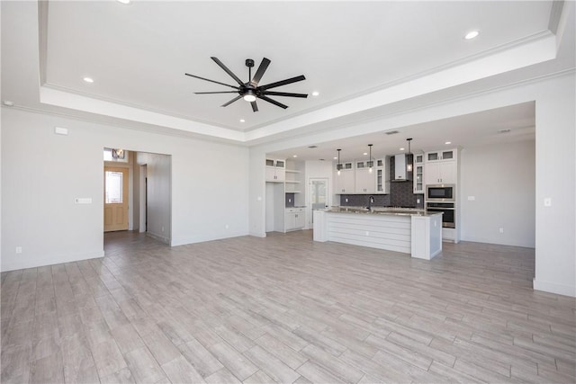 unfurnished living room with a raised ceiling, ceiling fan, crown molding, and light hardwood / wood-style floors