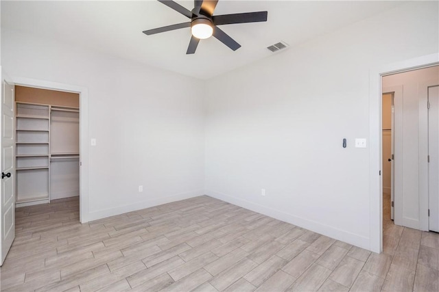 unfurnished bedroom with a walk in closet, ceiling fan, a closet, and light hardwood / wood-style flooring