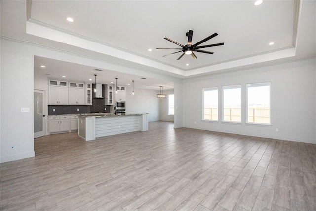 unfurnished living room featuring ceiling fan, a raised ceiling, light wood-type flooring, and crown molding