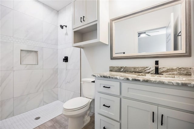 bathroom with hardwood / wood-style floors, vanity, toilet, and a tile shower