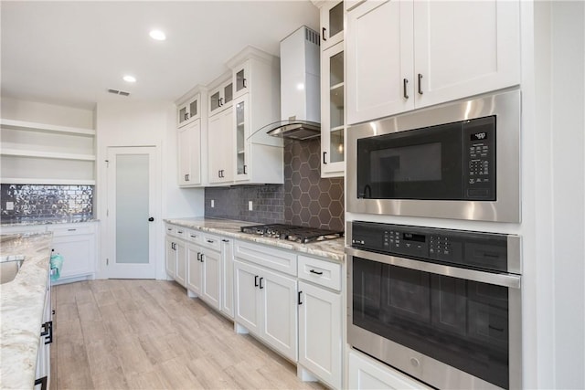 kitchen with white cabinets, light stone counters, wall chimney exhaust hood, and stainless steel appliances