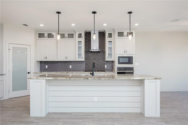 kitchen with white cabinets, light stone counters, wall chimney range hood, and appliances with stainless steel finishes