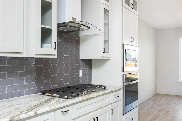 kitchen with backsplash, white cabinetry, stainless steel appliances, and wall chimney range hood