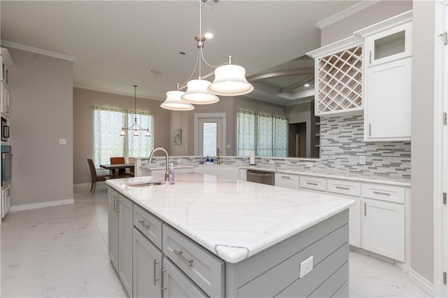 kitchen with sink, backsplash, ornamental molding, light stone countertops, and an island with sink