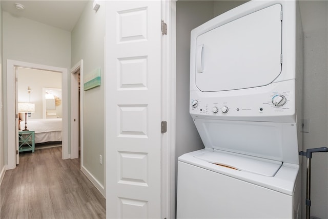 laundry room with stacked washing maching and dryer and light hardwood / wood-style floors