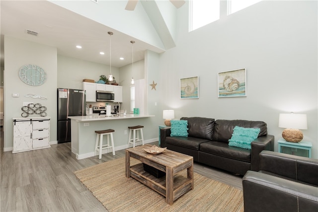 living room with ceiling fan, light wood-type flooring, and a towering ceiling