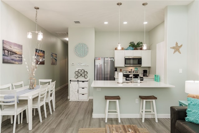 kitchen with white cabinets, a kitchen breakfast bar, light hardwood / wood-style floors, kitchen peninsula, and stainless steel appliances