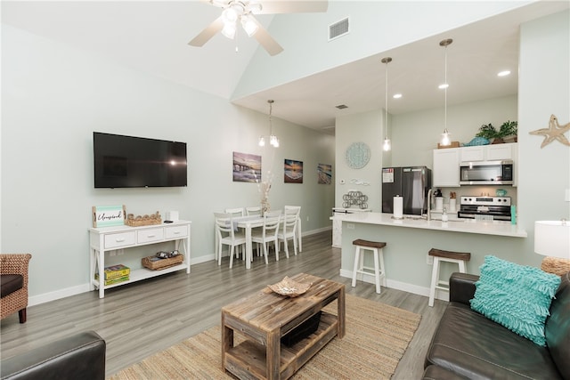 living room featuring hardwood / wood-style flooring, high vaulted ceiling, ceiling fan, and sink