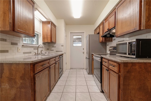 kitchen featuring stainless steel appliances, light stone counters, sink, light tile patterned flooring, and backsplash