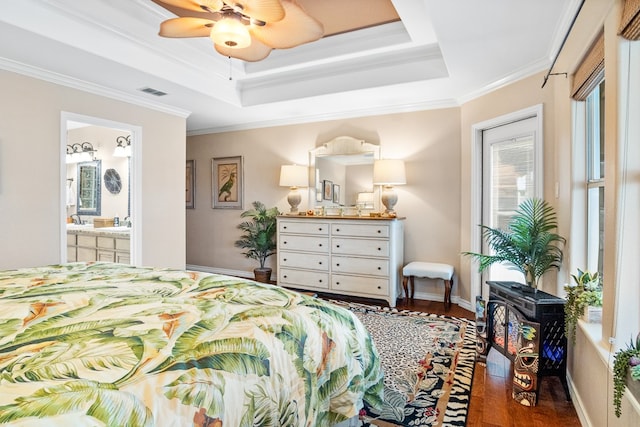 bedroom with ornamental molding, connected bathroom, a raised ceiling, dark hardwood / wood-style flooring, and ceiling fan