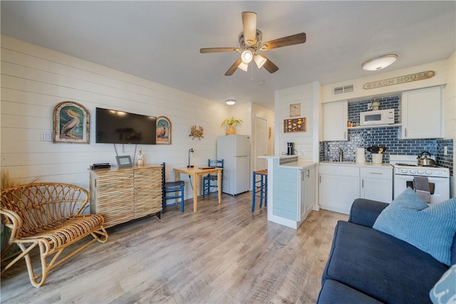 living room with light wood-style floors, visible vents, and ceiling fan