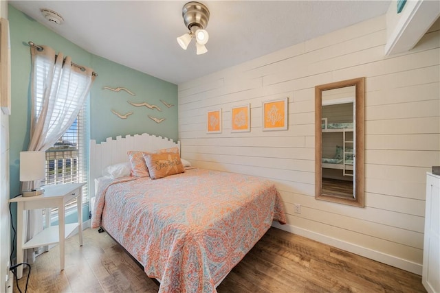 bedroom with wood walls, baseboards, and dark wood-style flooring