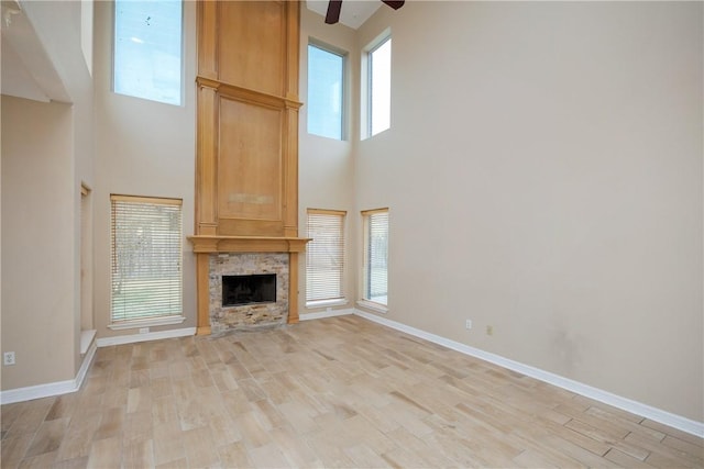 unfurnished living room featuring ceiling fan, light hardwood / wood-style floors, a towering ceiling, and a fireplace