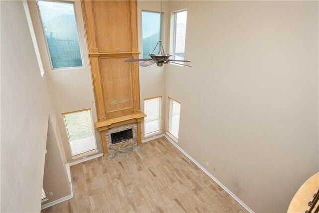 unfurnished living room with light hardwood / wood-style flooring, plenty of natural light, a stone fireplace, and ceiling fan