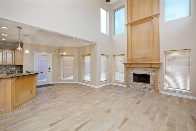 unfurnished living room featuring sink, an inviting chandelier, light hardwood / wood-style flooring, a fireplace, and a high ceiling