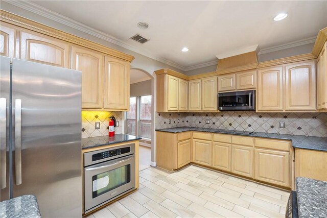 kitchen with decorative backsplash, ornamental molding, stainless steel appliances, light brown cabinets, and dark stone countertops