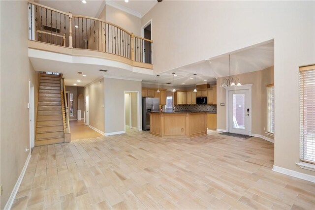 unfurnished living room with a towering ceiling, an inviting chandelier, light hardwood / wood-style flooring, and crown molding