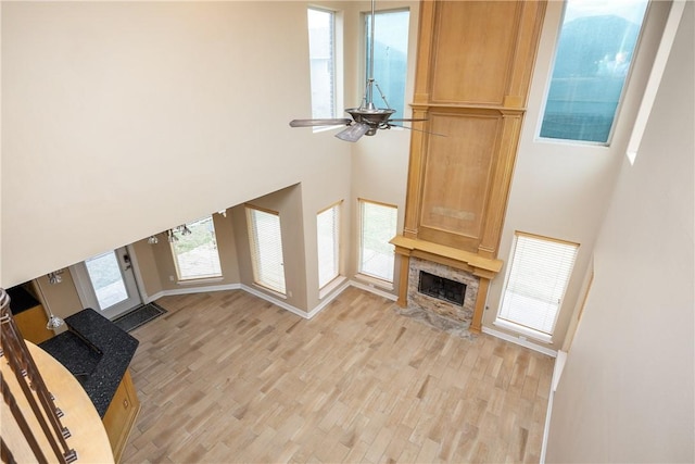 unfurnished living room with ceiling fan, light wood-type flooring, a high ceiling, and a high end fireplace