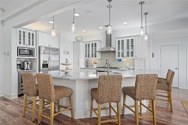 kitchen with appliances with stainless steel finishes, a breakfast bar area, white cabinets, decorative backsplash, and wall chimney range hood