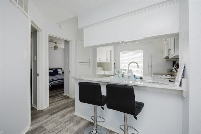 kitchen featuring a kitchen breakfast bar, white cabinetry, light hardwood / wood-style flooring, and kitchen peninsula