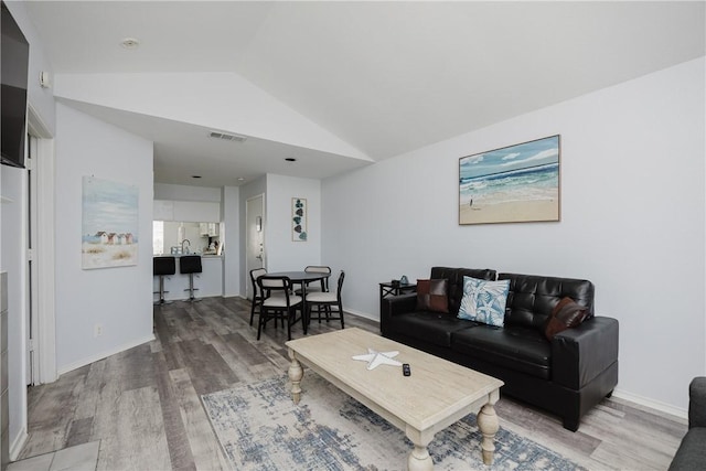 living area featuring lofted ceiling, light wood-style floors, and baseboards