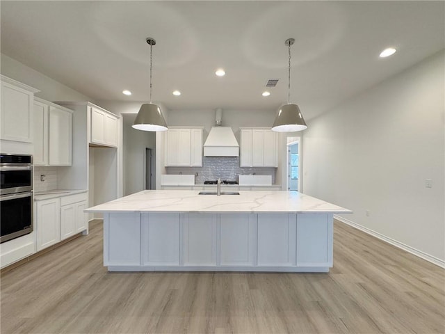 kitchen with visible vents, an island with sink, white cabinetry, and custom range hood