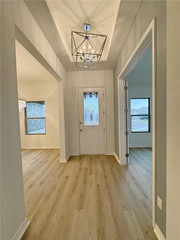 entrance foyer with light wood-type flooring, a raised ceiling, a notable chandelier, and baseboards