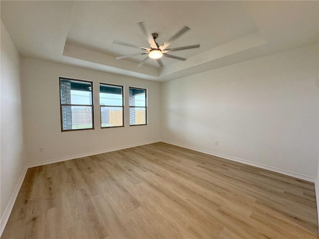 empty room featuring light wood-style floors, baseboards, a tray ceiling, and a ceiling fan