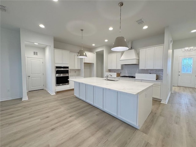 kitchen with visible vents, a center island with sink, white cabinetry, and stainless steel double oven