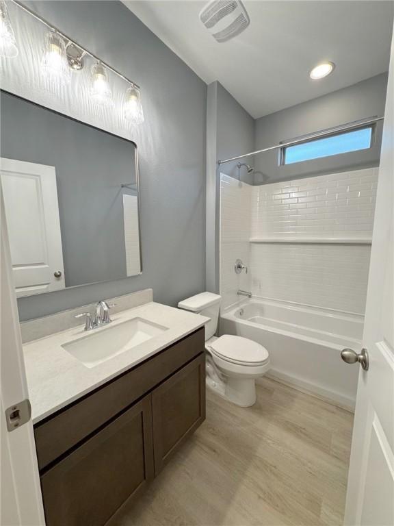 bathroom with visible vents, toilet, wood finished floors, vanity, and washtub / shower combination