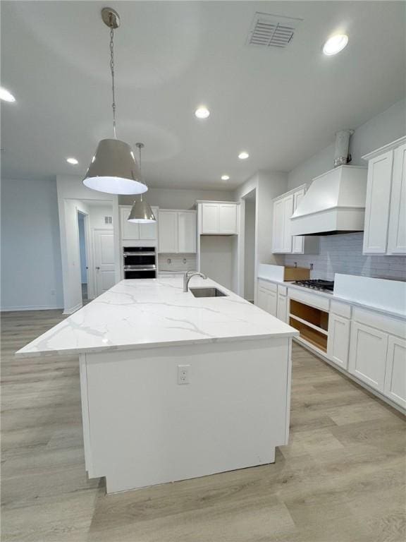 kitchen with a kitchen island with sink, visible vents, and white cabinets