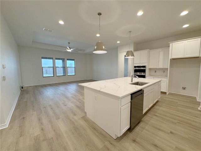 kitchen with light stone countertops, black dishwasher, a center island with sink, and white cabinets