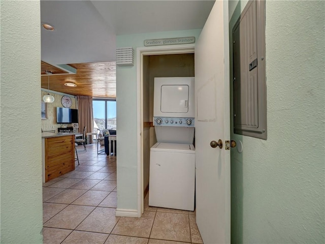 laundry room with laundry area, electric panel, light tile patterned flooring, stacked washer and dryer, and a textured wall