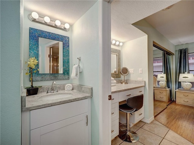 full bath with a textured ceiling, two vanities, tile patterned flooring, and a sink