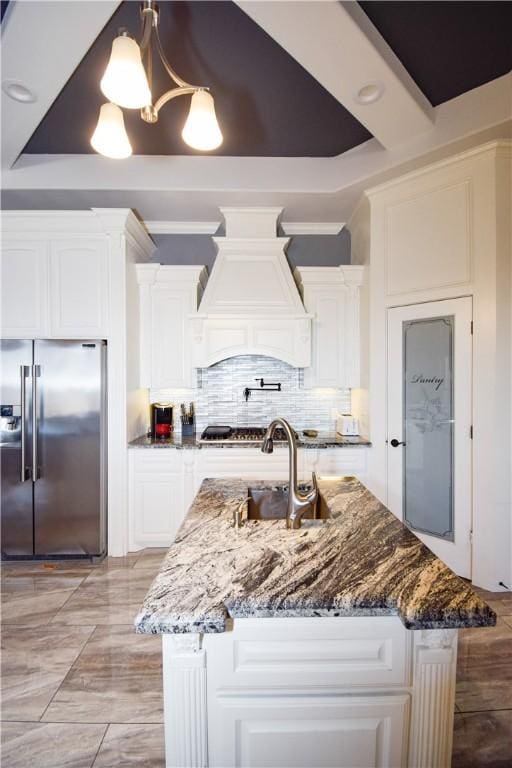 kitchen featuring appliances with stainless steel finishes, dark stone counters, custom exhaust hood, decorative light fixtures, and an island with sink