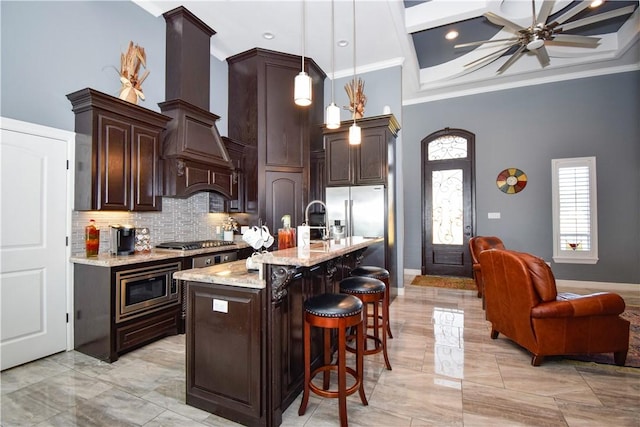 kitchen with dark brown cabinetry, a kitchen breakfast bar, decorative light fixtures, a center island with sink, and custom range hood