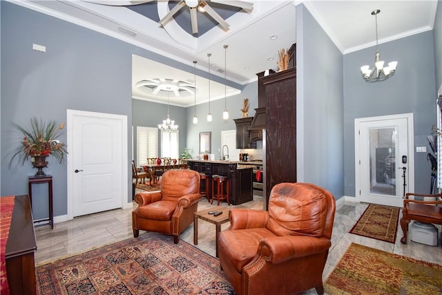 living room with a towering ceiling, ceiling fan with notable chandelier, crown molding, sink, and light tile patterned floors