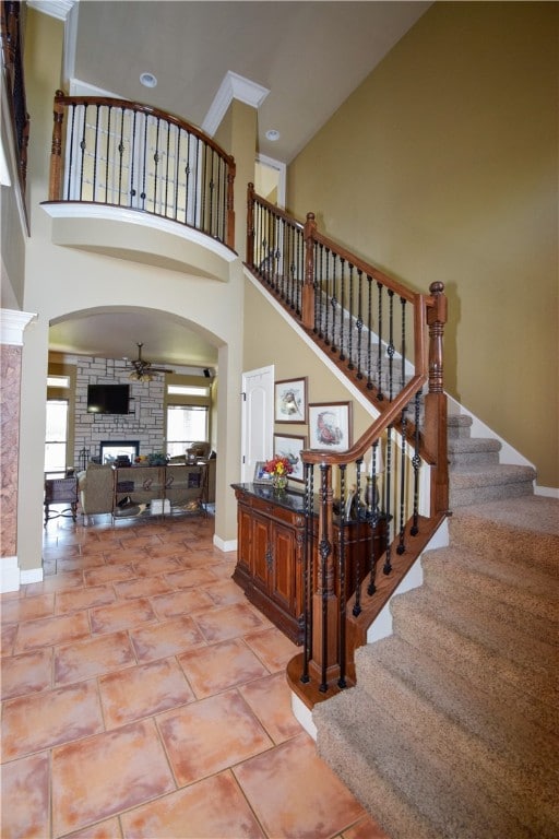 stairs featuring tile patterned flooring, crown molding, a towering ceiling, and a fireplace