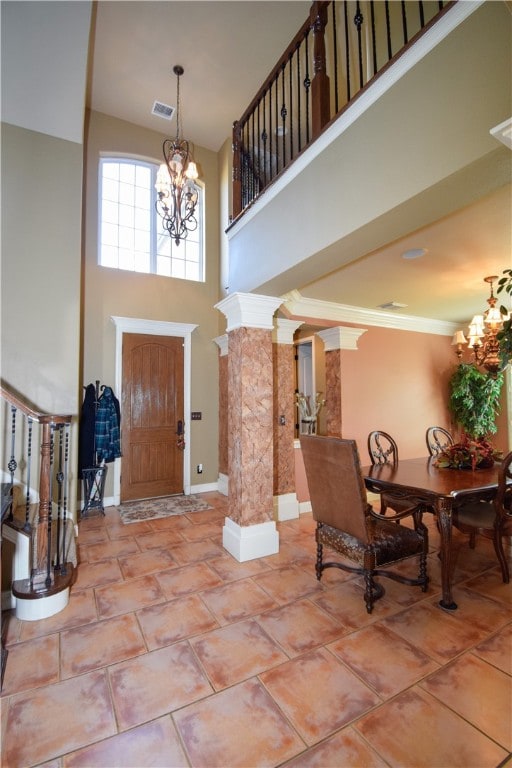 tiled foyer featuring a towering ceiling, ornate columns, ornamental molding, and a notable chandelier