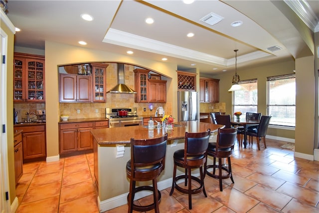 kitchen with sink, wall chimney exhaust hood, tasteful backsplash, a center island with sink, and appliances with stainless steel finishes