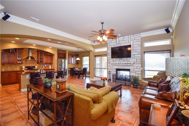 tiled living room with ceiling fan, a fireplace, and ornamental molding