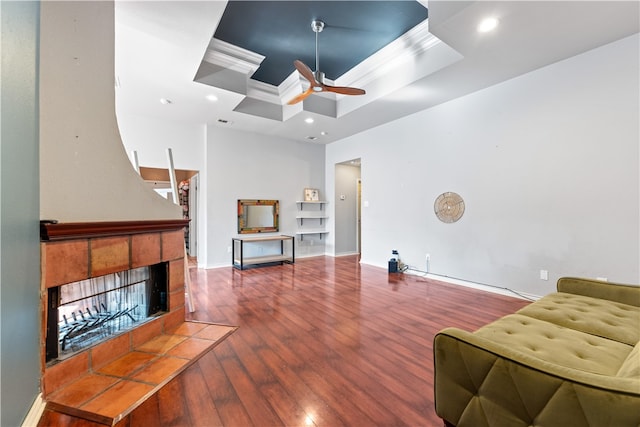 living room with ceiling fan, hardwood / wood-style floors, a fireplace, a raised ceiling, and crown molding