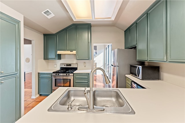 kitchen featuring vaulted ceiling, green cabinets, sink, light tile patterned floors, and appliances with stainless steel finishes