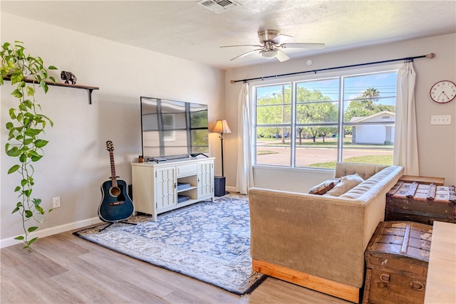 living room with a textured ceiling, light wood-type flooring, and ceiling fan