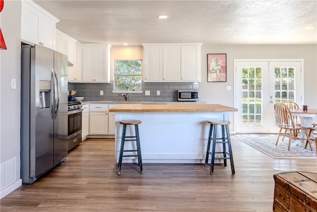 kitchen featuring butcher block counters, white cabinetry, a breakfast bar, and stainless steel appliances