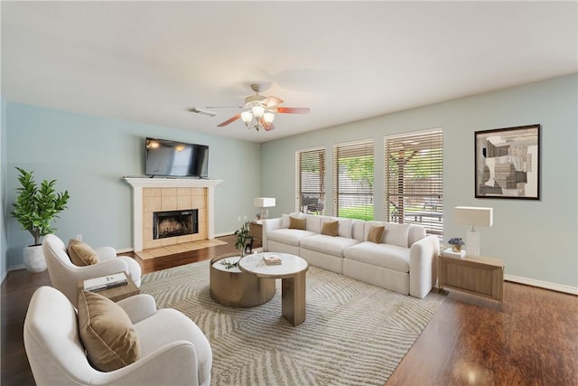 living room with a ceiling fan, visible vents, wood finished floors, and a tile fireplace