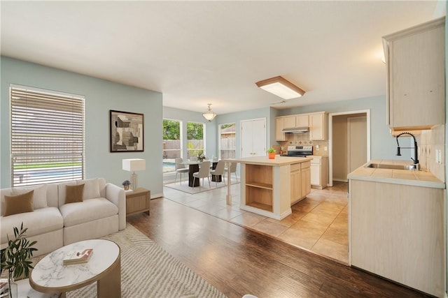kitchen featuring a sink, light wood-style floors, tasteful backsplash, under cabinet range hood, and stainless steel electric stove