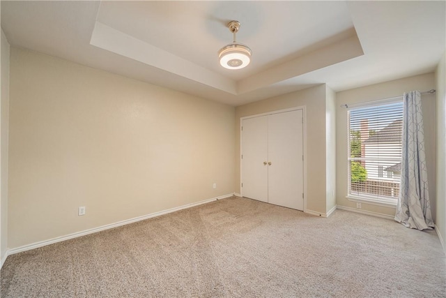 unfurnished bedroom with baseboards, a tray ceiling, and light colored carpet