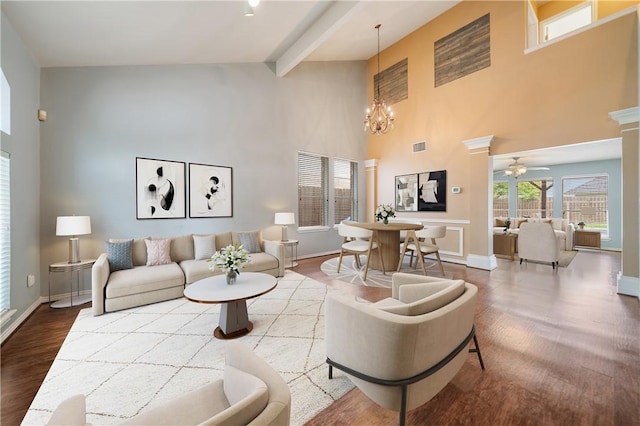 living room with a high ceiling, ceiling fan with notable chandelier, baseboards, wood finished floors, and beamed ceiling