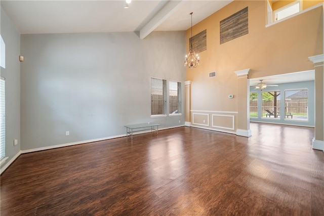 unfurnished room featuring a towering ceiling, wood finished floors, baseboards, beamed ceiling, and ceiling fan with notable chandelier